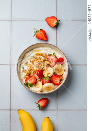 Natural Greek yogurt with granola, banana and strawberries in a bowl on a tile background Natural Greek yogurt with granola, banana and strawberries in a bowl on a tile background 140834976