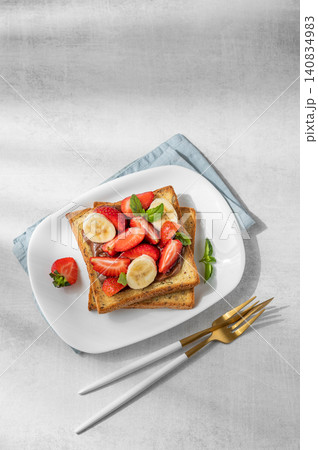 Toasted bread with chocolate cream, strawberries, and banana on a plate on a concrete background 140834983