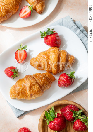 Freshly baked croissants on a plate with strawberries on a bright textured background. 140834999