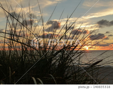 Scenic sunset view over the ocean through beach grass silhouettes. Scenic sunset view over the ocean through beach grass silhouettes. 140835318