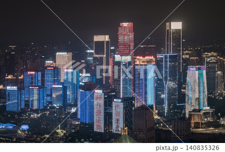 At night, Chongqing becomes a futuristic wonderland of light and shadow. Towering skyscrapers pierce the sky, their glass facades shimmering with cascading LEDs. Vibrant ribbons of neon bleed into the 140835326