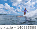 Youthful Woman Maintains Balance On Longboard Near Peaceful Coastlines 140835599