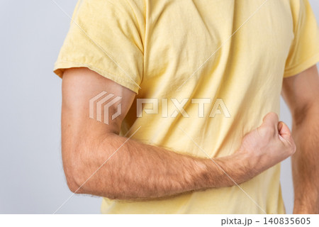 Man wearing a yellow t shirt clenching his fist behind his back, highlighting muscular arm and biceps, representing pain, injury, strength, or stretching discomfort Man wearing a yellow t shirt clenching his fist behind his back, highlighting muscular arm and biceps, representing pain, injury, strength, or stretching discomfort 140835605