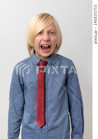 Blonde haired boy wearing a blue denim shirt and red tie, screaming with an open mouth, expressing strong emotions like anger, frustration and stress 140835753