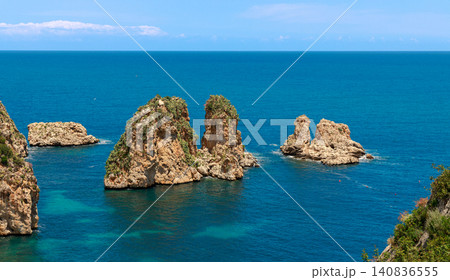 Jagged rock formations covered in greenery emerge from the vibrant blue sea, showcasing a rugged coastal landscape perfect for travel inspiration Jagged rock formations covered in greenery emerge from the vibrant blue sea, showcasing a rugged coastal landscape perfect for travel inspiration 140836555