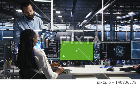 Female software programmer talking with team supervisor in high tech server room, checks AI diagnostics on chroma key computer. 140836579