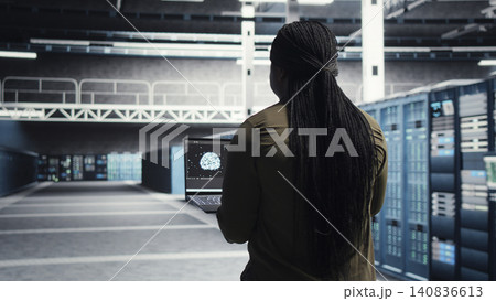 Data center engineer uses laptop in a server room to monitor AI diagnostics and neural network performance. 140836613