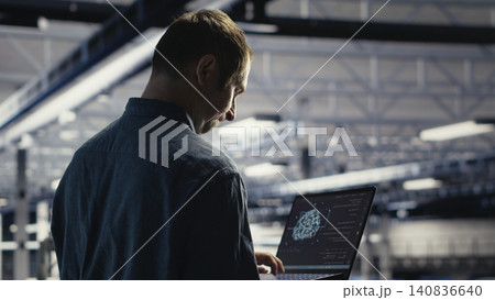 Technician monitors server room activity working with laptop while walking through facility. 140836640