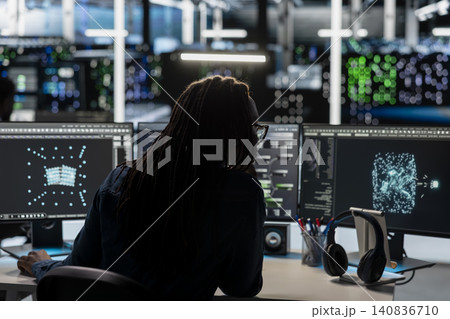 Woman programmer reviews an AI visualization dashboard on a PC in a server farm to find equipment issues and reduce hardware failures. 140836710