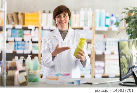 Female pharmacist behind counter recommending therapeutic shampoo Female pharmacist behind counter recommending therapeutic shampoo 140837701