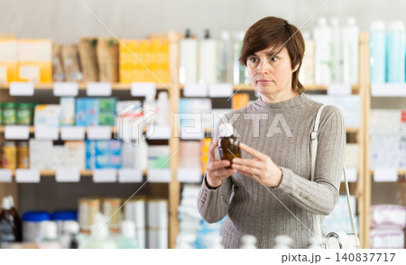 Middle-aged woman examining bottle of fever-reducing syrup in pharmacy Middle-aged woman examining bottle of fever-reducing syrup in pharmacy 140837717