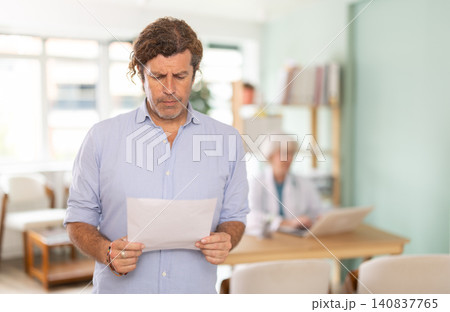 Distressed man looking at test results in medical office Distressed man looking at test results in medical office 140837765