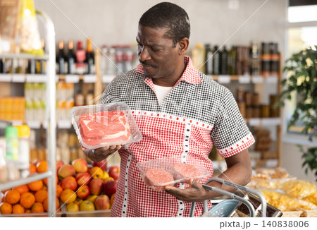 African man in store took raw beef steaks and hamburger cutlet, choose meat ware African man in store took raw beef steaks and hamburger cutlet, choose meat ware 140838006
