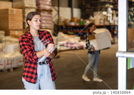 Attentive female manager keeps records of bulk construction materials in warehouse, writing down the data on paper Attentive female manager keeps records of bulk construction materials in warehouse, writing down the data on paper 140838064