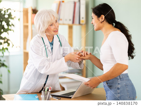 Elderly female doctor shaking hands with woman patient at table 140838170