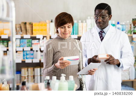 Woman choose buy painkiller tablet at pharmacy. African man in background Woman choose buy painkiller tablet at pharmacy. African man in background 140838200