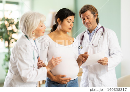 Happy pregnant woman discussing medical test results with two doctors Happy pregnant woman discussing medical test results with two doctors 140838217