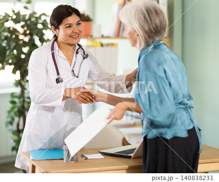 Female doctor shaking hands with elderly woman patient at table Female doctor shaking hands with elderly woman patient at table 140838231