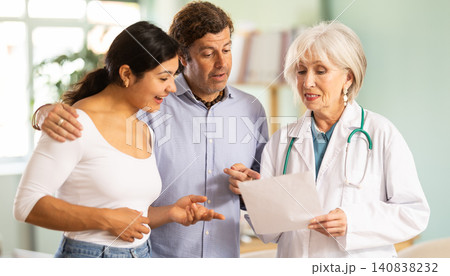Elderly doctor discussing medical tests with happy couple in medical office Elderly doctor discussing medical tests with happy couple in medical office 140838232