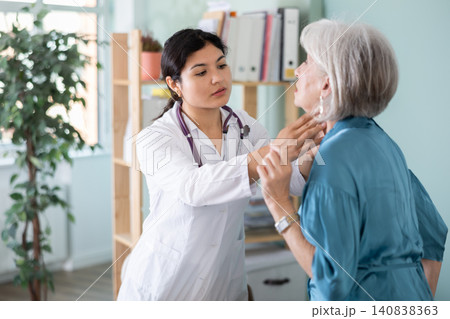Senior woman holds sore spot one sore throat at doctors appointment Senior woman holds sore spot one sore throat at doctors appointment 140838363