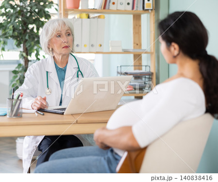 Elderly female doctor talking with pregnant patient at table 140838416