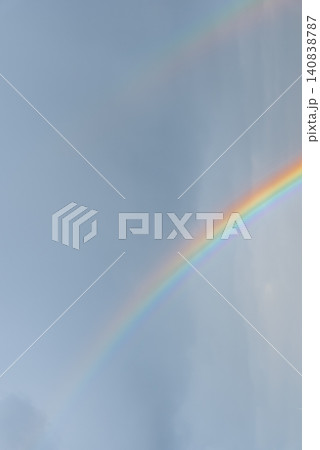 Colorful Rainbow Across Blue Cloudy Sky After Rain. Vibrant rainbow stretches across blue sky filled with soft clouds after rainfall. The colorful atmospheric phenomenon creates striking natural scene Colorful Rainbow Across Blue Cloudy Sky After Rain. Vibrant rainbow stretches across blue sky filled with soft clouds after rainfall. The colorful atmospheric phenomenon creates striking natural scene 140838787