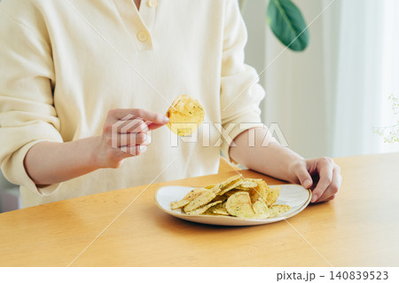 家でポテトチップスを食べる若い女性の手元 140839523