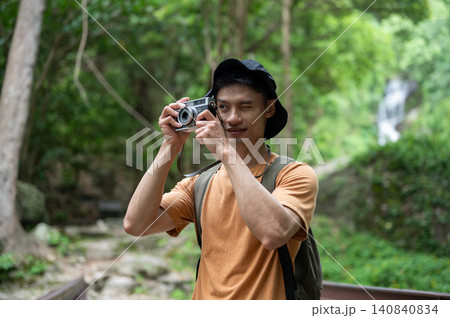 Asian man traveler captures the view on camera while exploring lush green forest on mountain trail. 140840834