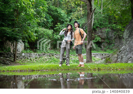 Asian man and woman hikers travelers explore a lush forest and reflective pond on a mountain trail Asian man and woman hikers travelers explore a lush forest and reflective pond on a mountain trail 140840839