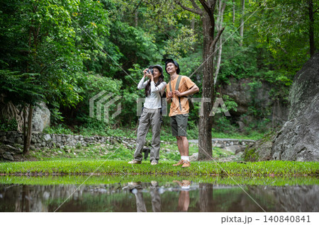 Asian female photographer and male traveler enjoying beside a reflective pond on a mountain trail Asian female photographer and male traveler enjoying beside a reflective pond on a mountain trail 140840841