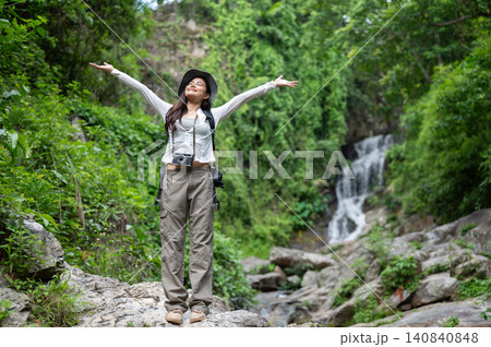 Happy asian woman tourist raising both arms standing on waterfall's rocks in forest on hiking trail. Happy asian woman tourist raising both arms standing on waterfall's rocks in forest on hiking trail. 140840848