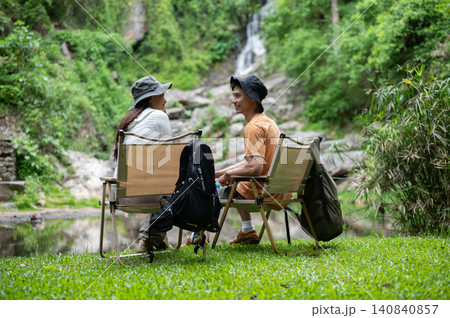 Asian male and female travelers relaxing by waterfall after hiking through forest on mountain trail. Asian male and female travelers relaxing by waterfall after hiking through forest on mountain trail. 140840857