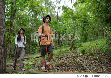 Asian male and female companion hikers explore a path in green tropical forest on a mountain trail Asian male and female companion hikers explore a path in green tropical forest on a mountain trail 140840879