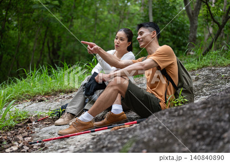 Asian male and female hikers resting, pointing and enjoying forest views together on mountain trail Asian male and female hikers resting, pointing and enjoying forest views together on mountain trail 140840890