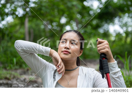 Pretty asian woman tourist holding trekking staff wiping sweat in forest while going on hiking trail 140840901