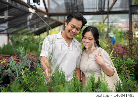 Asian man and woman couple enjoying quality time among plants in a greenhouse nursery garden center. Asian man and woman couple enjoying quality time among plants in a greenhouse nursery garden center. 140841483