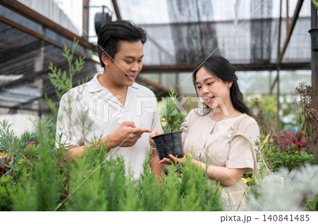 Asian man and woman couple selecting plants discussing gardening ideas in greenhouse nursery garden. Asian man and woman couple selecting plants discussing gardening ideas in greenhouse nursery garden. 140841485