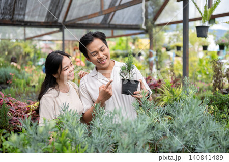 Asian man and woman couple selecting a potted plants for home decor in a greenhouse nursery garden. Asian man and woman couple selecting a potted plants for home decor in a greenhouse nursery garden. 140841489