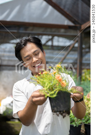 Close up of smiling asian man enjoying time with flowering plant in greenhouse nursery garden center Close up of smiling asian man enjoying time with flowering plant in greenhouse nursery garden center 140841530