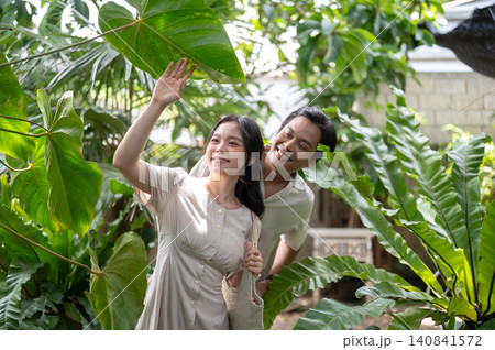 Happy asian man and woman couple exploring lush greenery while walking in a tropical garden at cafe 140841572
