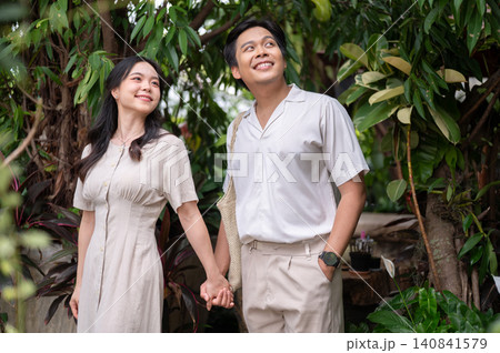 Asian man and woman couple admiring nature beauty holding hands walking together in tropical garden. 140841579