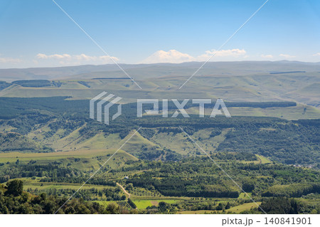 Panoramic view of the green valley and the snowy peak of Mount Elbrus on the horizon against the blue sky on a sunny clear morning in Kislovodsk Stavropol territory, Russia Panoramic view of the green valley and the snowy peak of Mount Elbrus on the horizon against the blue sky on a sunny clear morning in Kislovodsk Stavropol territory, Russia 140841901