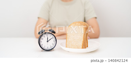 Happy smiling woman with whole wheat bread and alarm clock. concept of intermittent fasting, IF, meal timing, and choosing healthy carbohydrates for a balanced diet and weight loss management Happy smiling woman with whole wheat bread and alarm clock. concept of intermittent fasting, IF, meal timing, and choosing healthy carbohydrates for a balanced diet and weight loss management 140842124