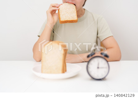 Happy smiling woman eating whole wheat bread with alarm clock. concept of intermittent fasting, IF, meal timing, and choosing healthy carbohydrates for a balanced diet and weight loss management Happy smiling woman eating whole wheat bread with alarm clock. concept of intermittent fasting, IF, meal timing, and choosing healthy carbohydrates for a balanced diet and weight loss management 140842129