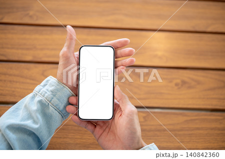 Close up of hand presenting empty screen smartphone over wooden surface for app branding and display Close up of hand presenting empty screen smartphone over wooden surface for app branding and display 140842360