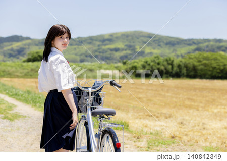 田園風景の中で自転車を押して振り返る女子高校生 田園風景の中で自転車を押して振り返る女子高校生 140842849