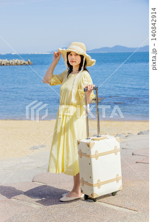 海辺のリゾートでスーツケースを持つ麦わら帽子の若い女性 140842914