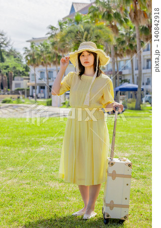 リゾートホテル前でスーツケースを持つ麦わら帽子の若い女性旅行者 140842918