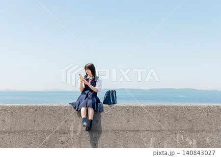 海辺の防波堤でスマートフォンを見る女子高校生 140843027