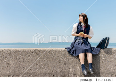 海辺の堤防に座りスマートフォンで音楽を楽しむ女子高校生 海辺の堤防に座りスマートフォンで音楽を楽しむ女子高校生 140843301